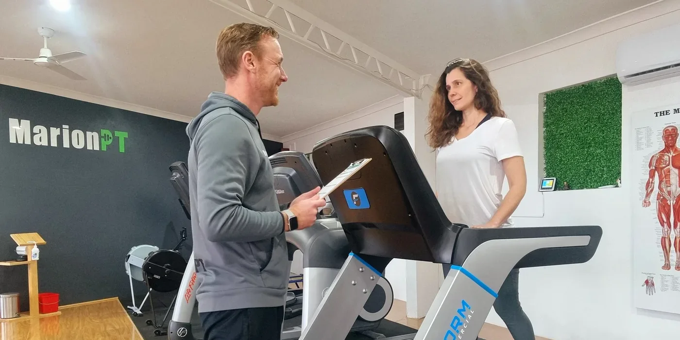 Henk with a clipboard talking to a client walking on a treadmill in the MarionPT studio
