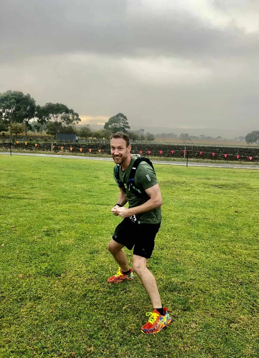 Henk running on the grass at the McLaren Vale course in race kit, fists clenched, grinning at the camera