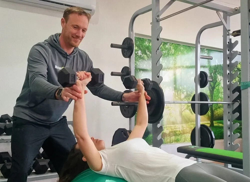 Henk supporting a client through a dumbbell press on a stability ball in the MarionPT studio