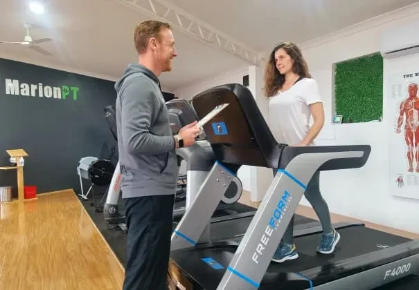 Henk with a clipboard talking to a client walking on a treadmill in the MarionPT studio