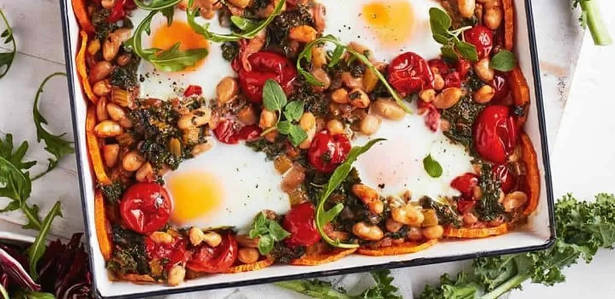 A sweet potato, bean and kale shakshuka in a baking dish with eggs baked into the top
