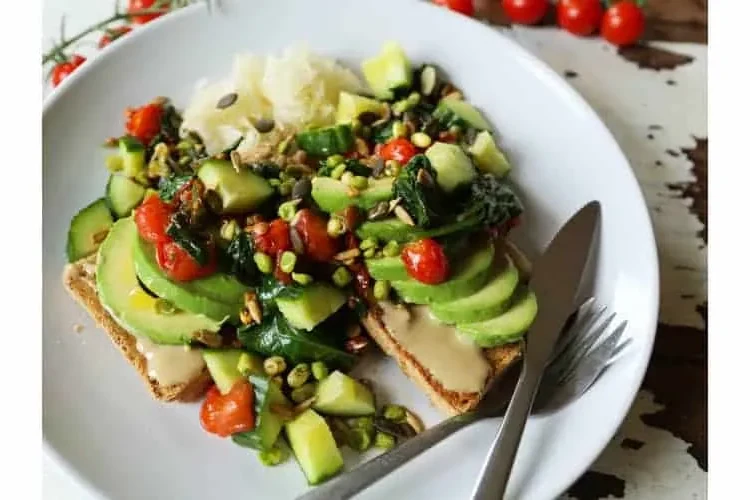 Toast loaded with spinach, cherry tomatoes, avocado, sauerkraut, sprouts and seeds