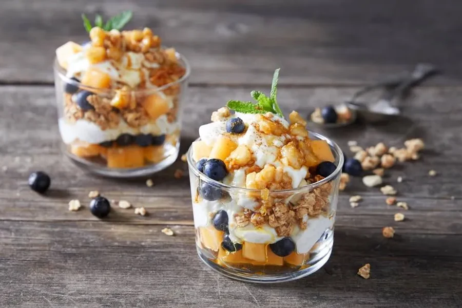 A layered parfait of coconut yoghurt, melon, blueberries and granola in a glass