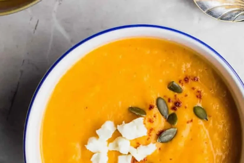 A bowl of creamy orange Thai sweet potato and carrot soup topped with pepitas