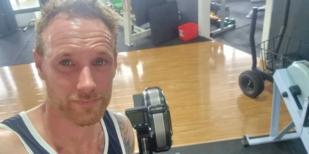 Henk, red-faced and sweating, taking a selfie beside a Concept2 rowing machine in the studio