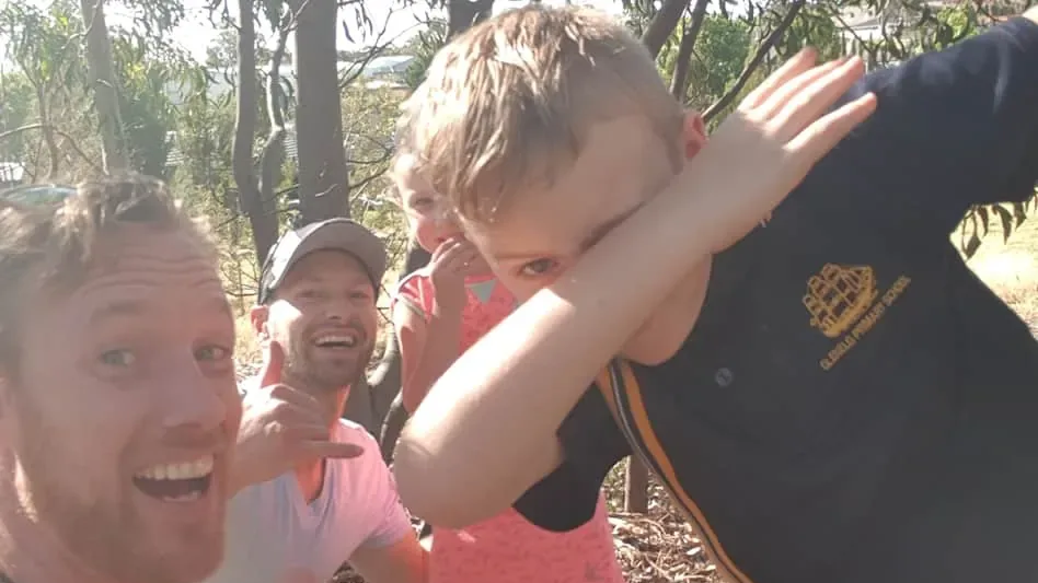 Henk and another adult crouching with two children among trees on a geocaching hunt