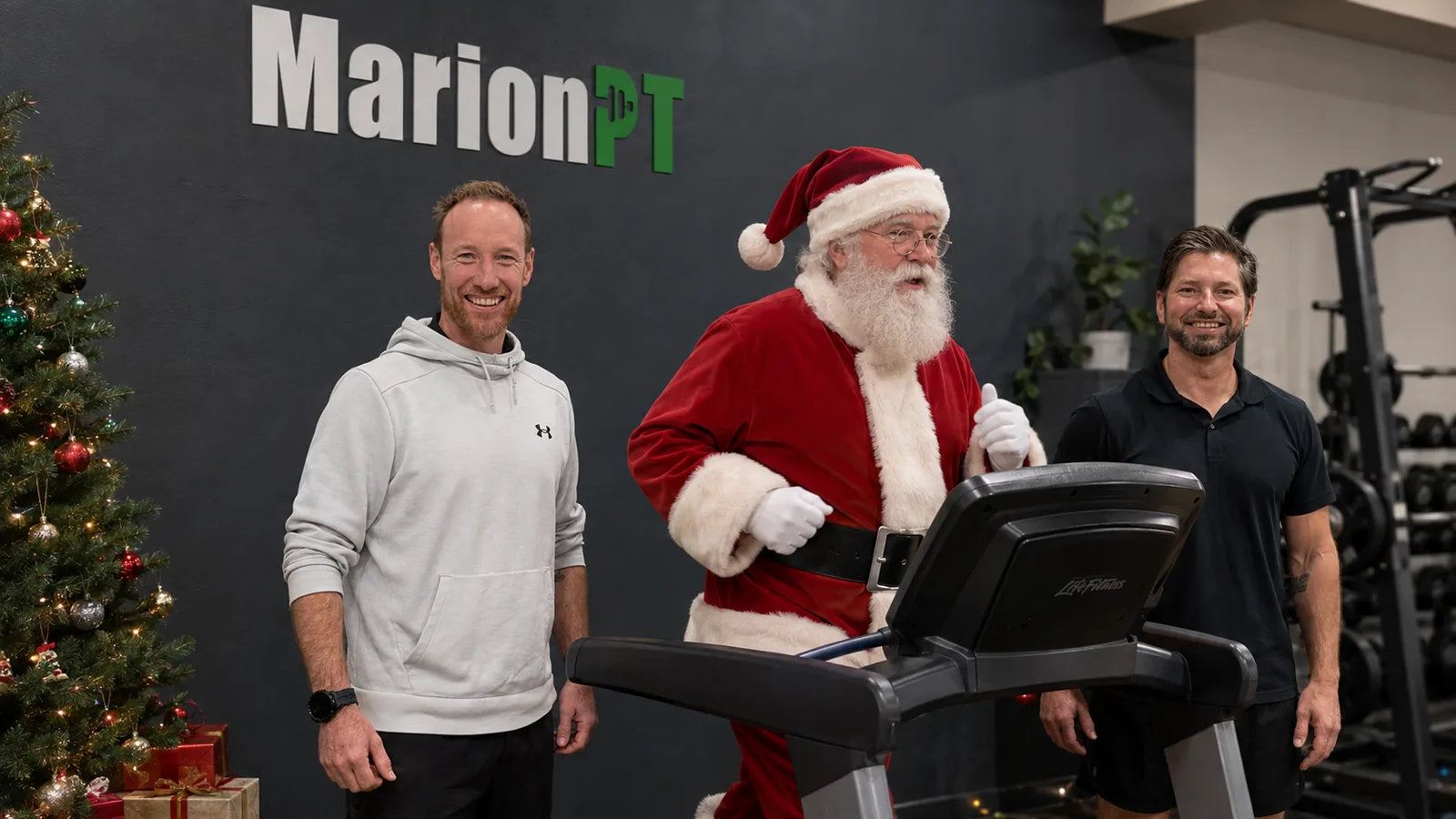 Two MarionPT trainers either side of Santa, who is running on a treadmill in the studio beside a decorated Christmas tree