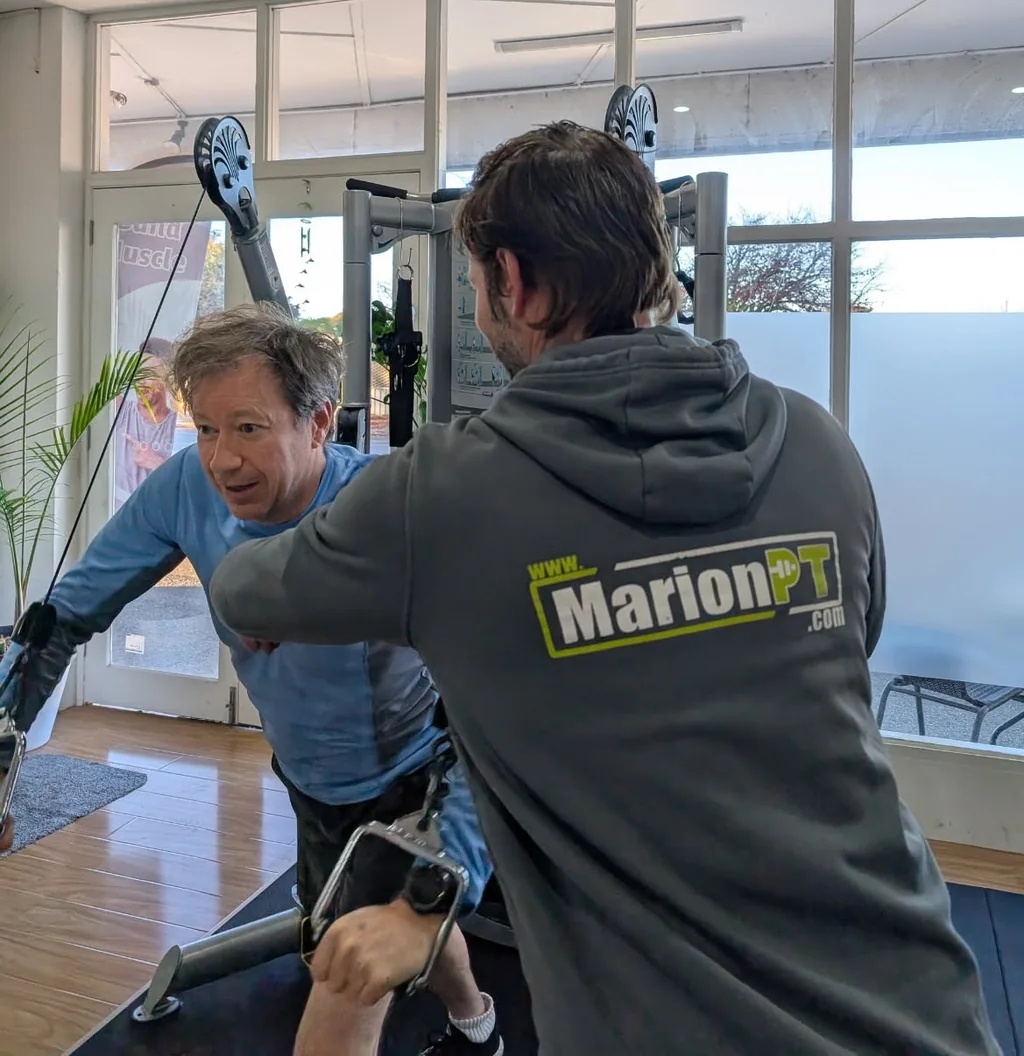 A MarionPT coach guiding Craig through a seated row in the Warradale studio