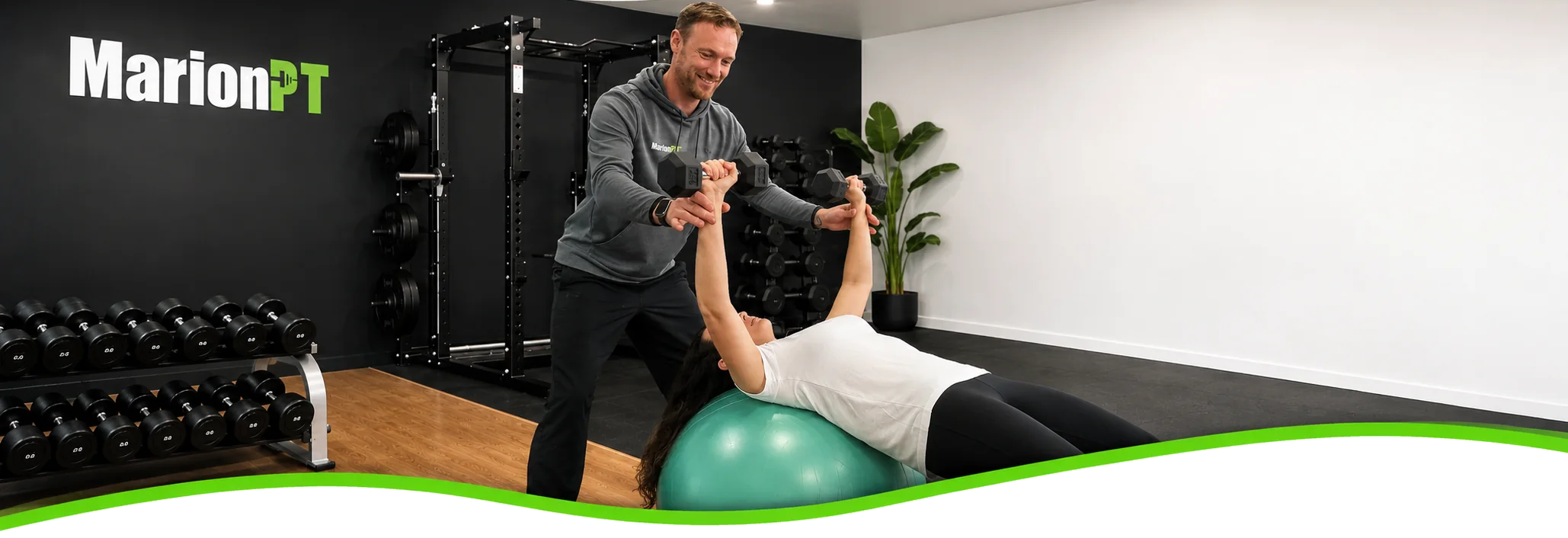 A MarionPT coach supporting a member through a dumbbell press on a stability ball in the Warradale studio